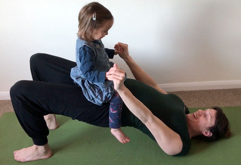 Yoga2shape kids' yoga class. Kat Frost balances two year old child on hips as she does Bridge Pose in a YogaShapes class